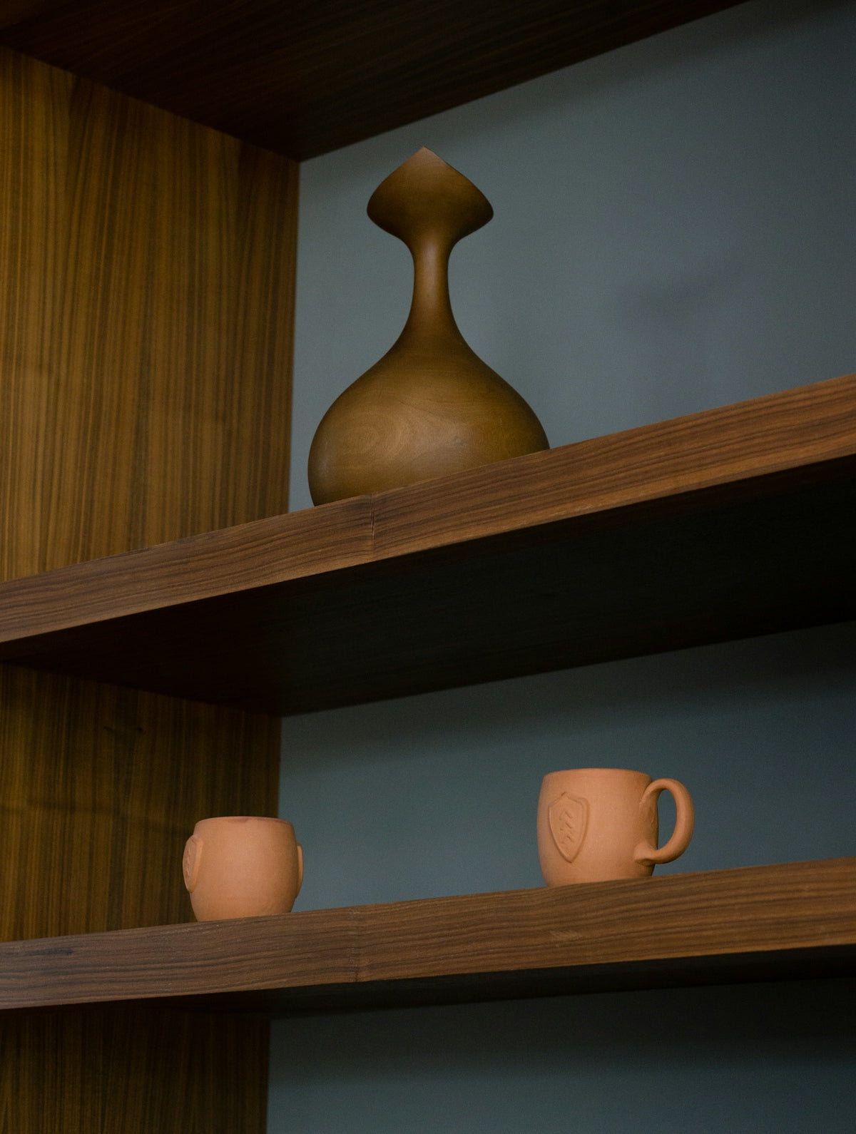 Decorative wooden vase and two terracotta mugs on shelves.